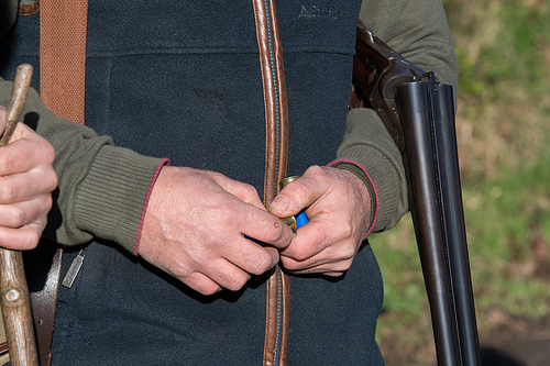 A man in shooting attire with a side-by-side 12 bore shotgun and cartridges