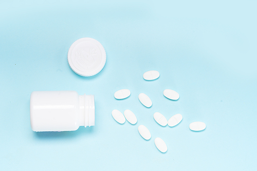 Pile of falling medical pills and white bottle on blue background, top view
