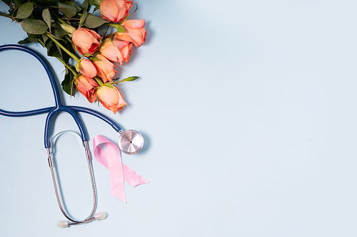 Pink ribbon, symbol of breast cancer awareness with stethoscope and flowers, copy space on blue background