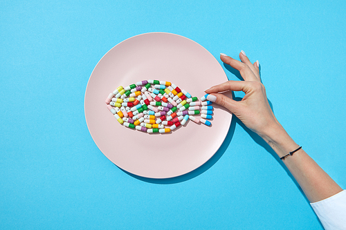 Many different pills and supplements as food on round white plate with woman's hand. Diet pills and supplements for dieting concept. Flat lay