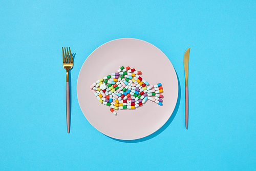 Many different pills and supplements as food on round white plate with fork and knife. Diet pills and supplements for dieting concept. Top view.