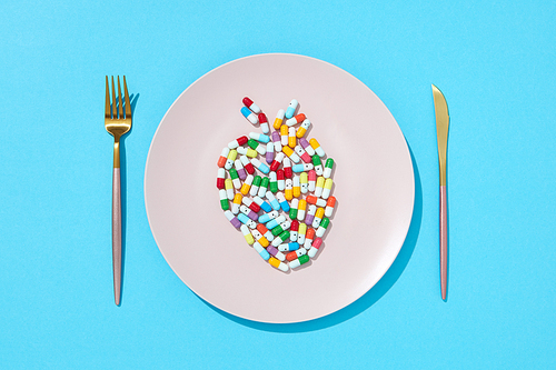 Different pills and supplements as food on round white plate in the form of fish on a blue background. Diet pills and supplements for dieting concept. Flat lay