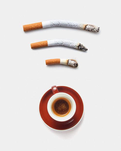 Three roach cigaretts around a cup of coffee as a wireless simbol on a light grey background with copy space. Concept of addiction from smoking and gadgets.
