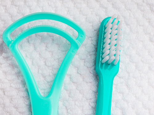 Oral hygiene health concept. Closeup dental tools green toothbrush and tongue cleaner on white towel