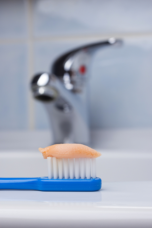Dental care health concept. Closeup blue brush toothbrush with paste in bathroom on sink, faucet in the background