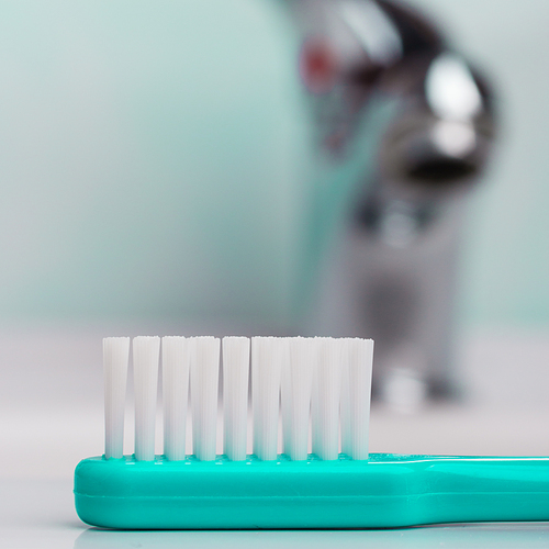 Dental care health concept. Closeup green brush toothbrush in bathroom on sink, faucet in the background