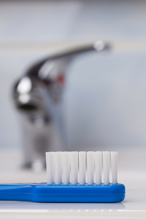 Dental care health concept. Closeup blue brush toothbrush in bathroom on sink, faucet in the background