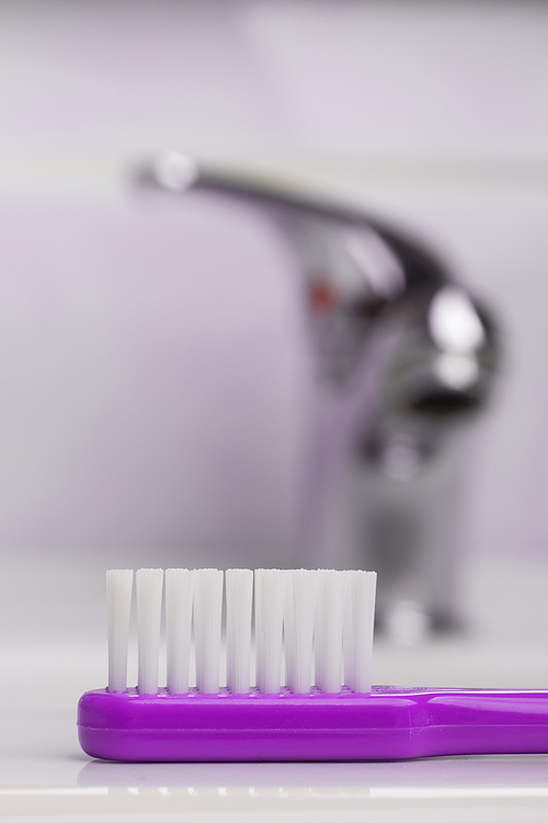Dental care health concept. Closeup violet brush toothbrush in bathroom on sink, faucet in the background