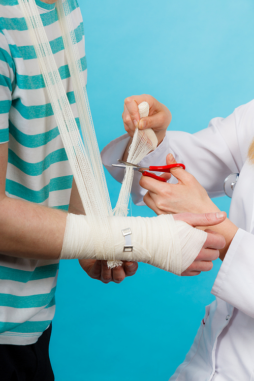 Medicine and healthcare. Female doctor bandaging male hand sprained wrist. Young man visiting medical professionalist.