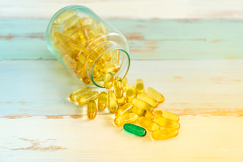 one green Pill medicine stand out from yellow pills and spilling out of pill bottle on vintage wooden background