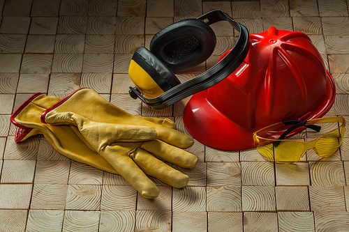construction safety tools leather gloves red helmet ggogles and earphones on wooden background
