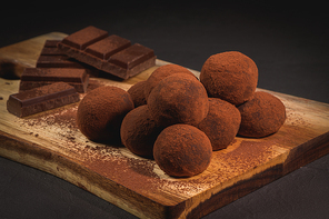 Craft chocolate truffles on wooden board with cocoa powder.