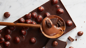wooden spoon with chocolate and chocolate balls on a white marble background