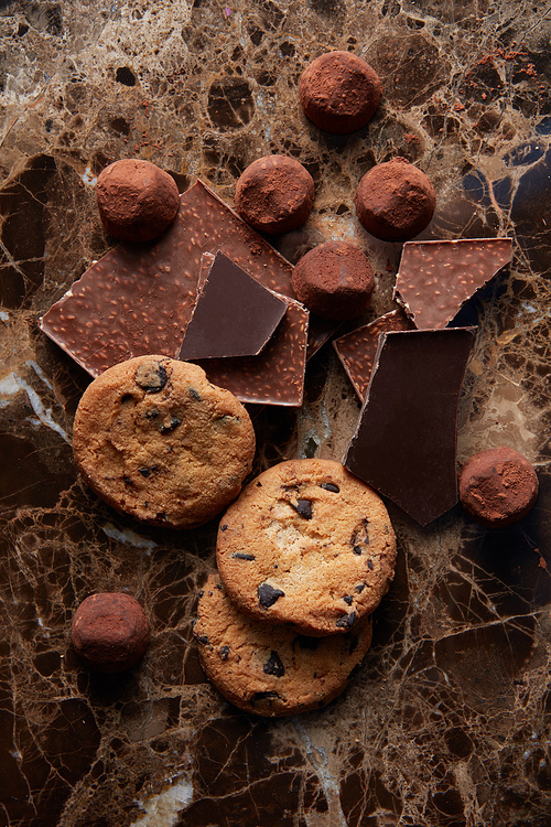 Chocolate chip cookies and different chocolate on cocoa powder and dark marble background