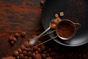 spoon with candies and cocoa powder in a sieve on a black plate, dark background with chocolate
