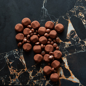 Assorted dark chocolate truffles with cocoa powder and biscuit on a dark marble background