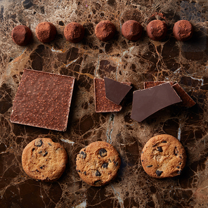 chocolate pieces, truffle candy and cookies on a marble dark background