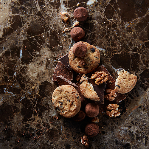 Fresh homemade chocolate chip cookies with chocolate candies in the dark marble background.