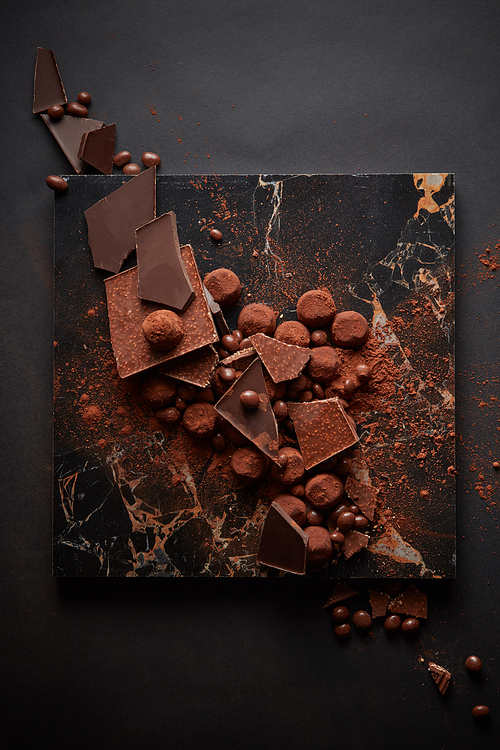 dark chocolate truffles in spilled cocoa powder on dark marble plate