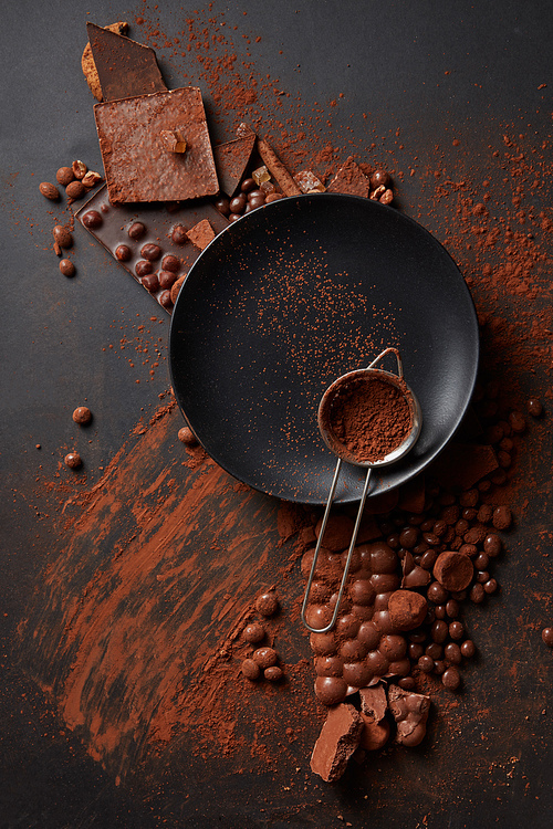 cocoa powder in a sieve on a black plate, dark background with chocolate