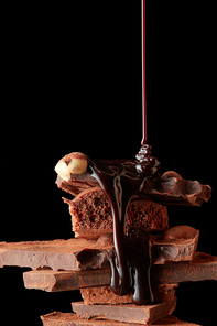 chocolate syrup being poured onto dark chocolate pieces isolated on black