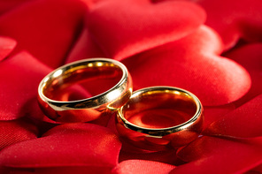 Two golden wedding rings on red hearts background