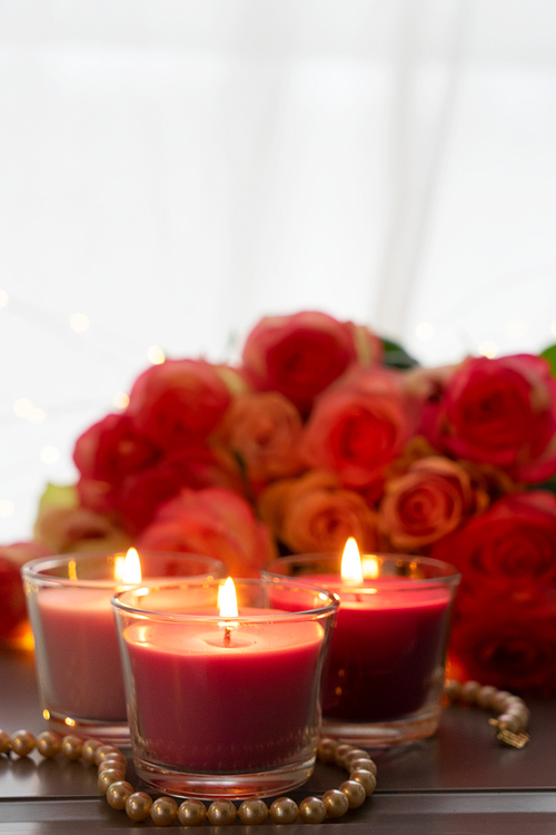 Glowing candles with rose fresh flowers bouquet on gray table, close up home interior details