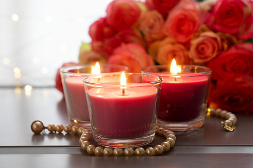 Burning candles with rose fresh flowers bouquet on gray table, close up home interior details
