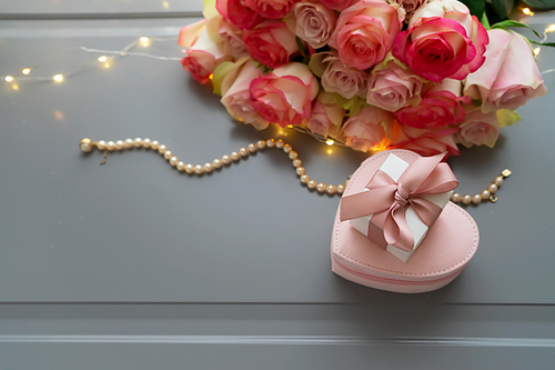Rose pink flowers bouquet with jewellery on gray table with gift box from above, flat lay scene