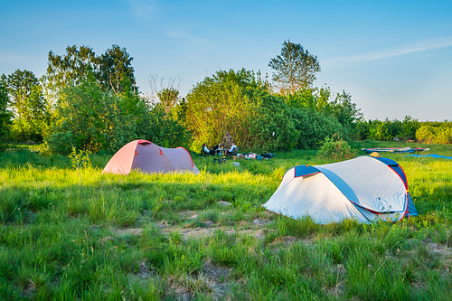 Tent camp camping at sunset on green grass field in forest and