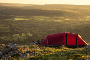 Beautiful image of wild camping in English countryside during stunning Summer sunrise with warm glow of the sun lighting the landscape
