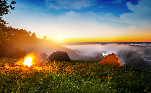 Tents and bonfire in steppe near river at sunrise