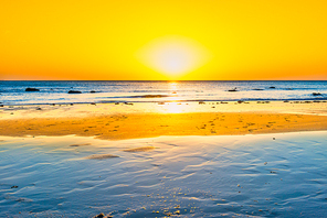 Sunset on beautiful sand beach with blue sea water and sun on sunset sky