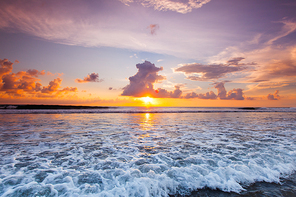 Sea waves at sandy beach at sunset, sun hiding behind a cloud