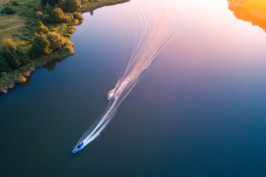 Aerial view of floating water scooter in blue water at sunset in summer. Holiday in countryside. Top view of boats in motion in the river. Landscape with moving motorboat and green trees. Extreme