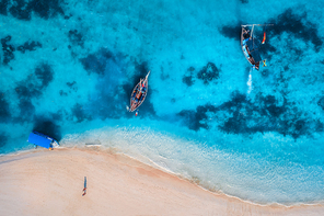 Aerial view of the fishing boats in clear azure water at sunrise in summer. Top view from drone of boat, blue sea, sandy beach, walking people. Indian ocean. Travel. Tropical seascape with motorboat