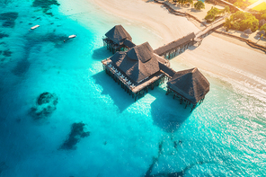 Aerial view of beautiful hotel on the water in ocean at sunset in summer. Zanzibar, Africa. Top view. Landscape with wooden hotel on the sea, azure water, sandy beach, green palm trees. Luxury resort