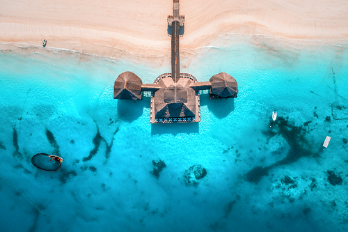 Aerial view of beautiful hotel in Indian ocean at sunset in summer. View from above.  Building on the transparent sea. Aerial seascape with wooden hotel, clear azure water, sandy beach. Luxury resort