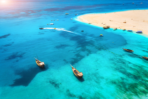 Aerial view of fishing boats and yachts on tropical sea coast with white sandy beach at summer evening. Indian Ocean in Africa. Colorful seascape with boat, transparent blue water at sunset. Top view