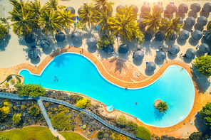 Aerial view of pool, umbrellas, sandy beach with green trees. Coast of Indian ocean at sunset in summer. Zanzibar, Africa. Top view. Landscape with azure water, parasols, palm trees. Luxury resort