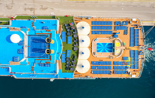 Aerial view of swimming pool, people on sunbeds, umbrellas on the cruise ship in summer. View from above of relaxing people on deck chairs, blue water in pool, wooden deck. Luxury cruise liner. Resort