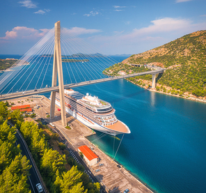 Aerial view of cruise ship and beautiful bridge in Dubrovnik, Croatia. Top view of large ship and road at sunset. Summer landscape with harbor, mountain, blue sea and green trees. Cruise liner in port