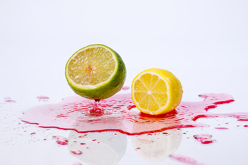 A lemon and lime are dropped onto red liquid making a splash.