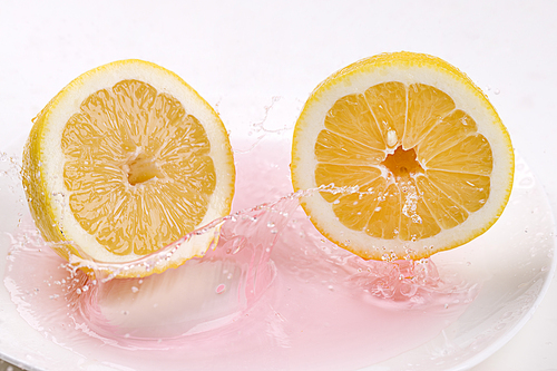 Two lemon halves are dropped into a plate with red tinted water making a splash.