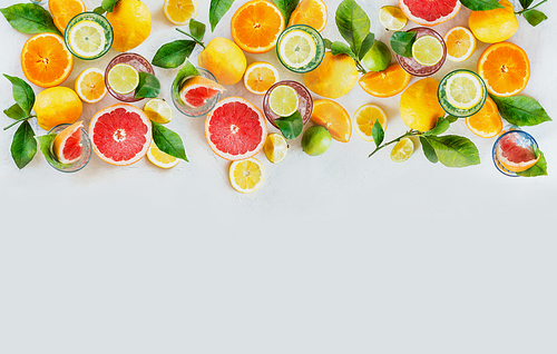 Various colorful citrus fruits: lemon, lime, orange and grapefruit with green leaves and glasses of refreshing lemonade drinks on white background, top view. Healthy lifestyle. Border or frame.