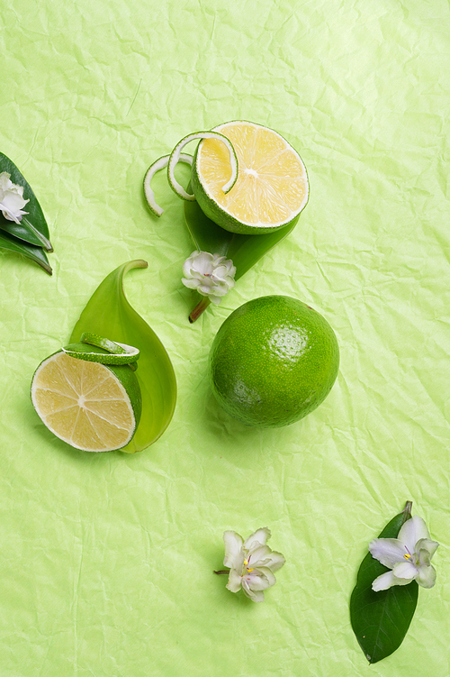 limes with leaves and flowers   on green background. flat lay. copy space