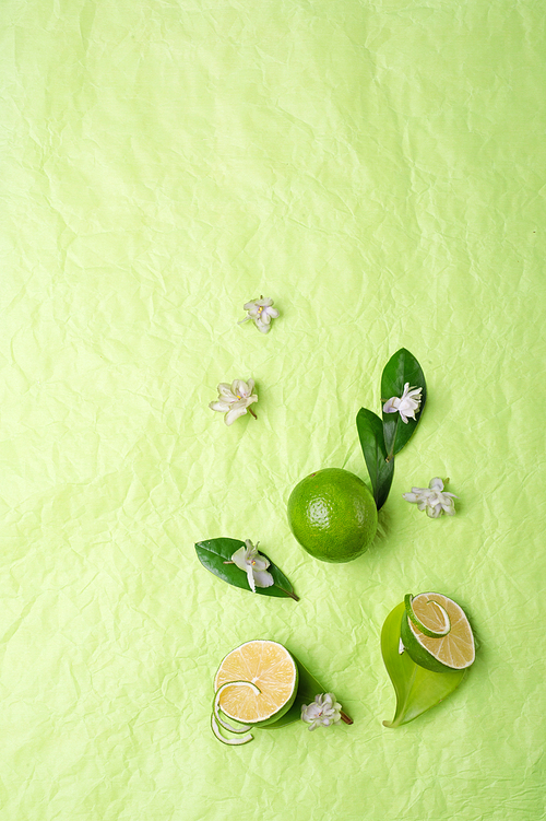 limes with leaves and flowers   on green background. flat lay. copy space