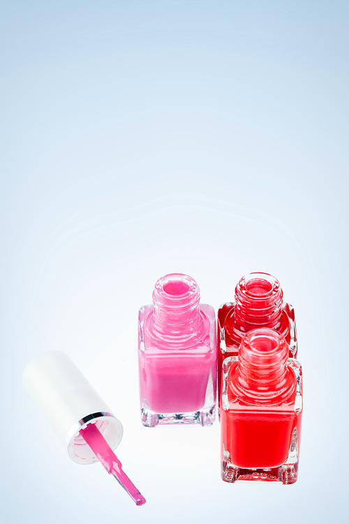 Three open nail polish bottles of different colors on a white surface with one pink brush.