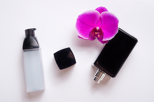 black fragrance  bottle with purple orchid and precious serum around white. flat lay