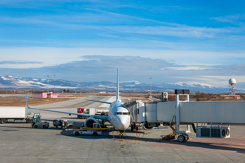 Airplane, jet airliner refueling with walkway attached and baggage being uploaded on the runway apron at Sofia Airport, Bulgaria, Europe during winter with snow on the ground